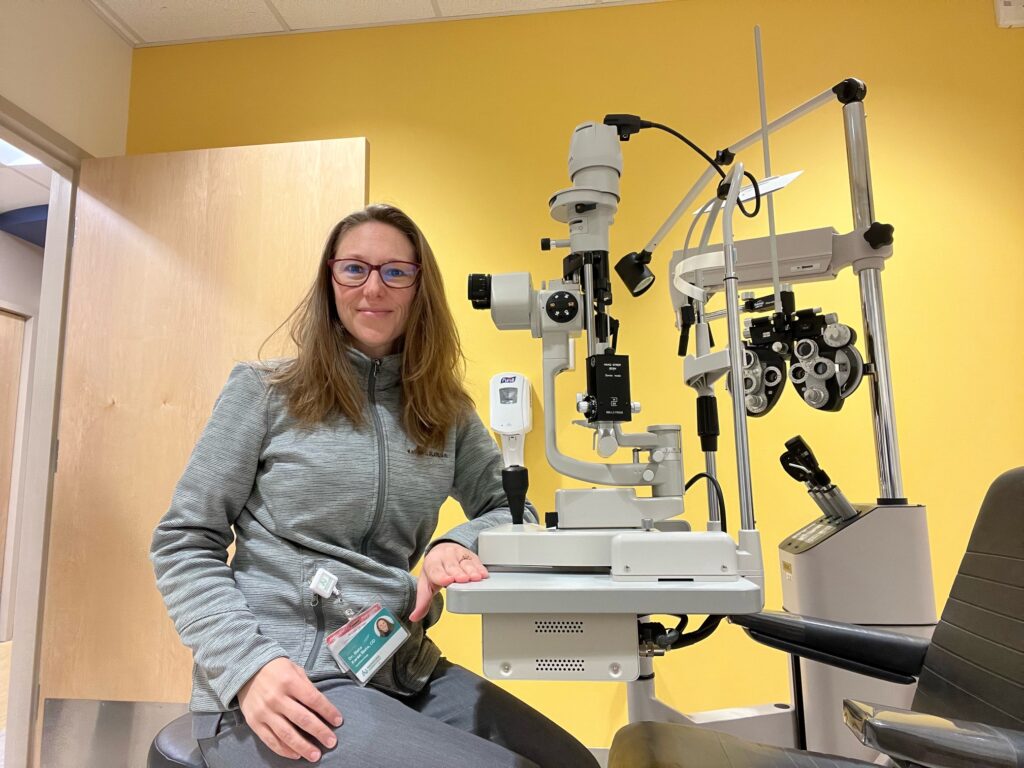 Dr. Karen Slate in gray jacket with at the slit lamp in nonprofit office with bright yellow walls